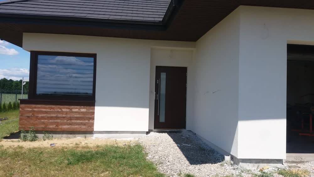 Parterowy dom z drewnianą okładziną przy wejściu, po wykonaniu elewacji
